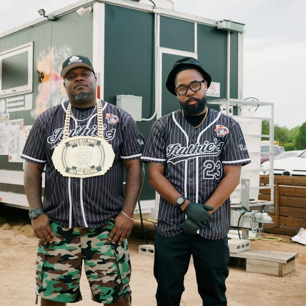Two men in Ruthie's baseball jerseys stand in front of a Ruthie's food truck.