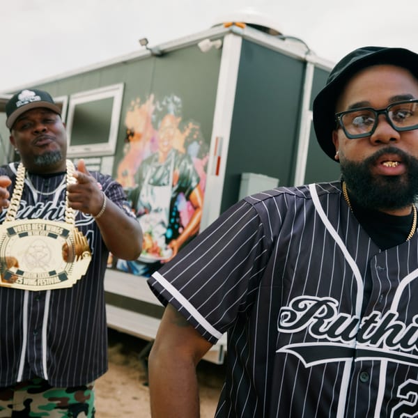 Two men in Ruthie's baseball jerseys pose in front of a food truck, one wearing a large gold chain.