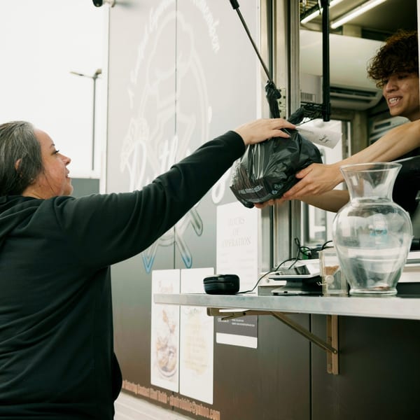 A customer receives a takeout order in a black bag from a food truck vendor.