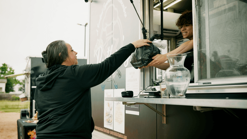 A customer receives a takeout order in a black bag from a food truck vendor.