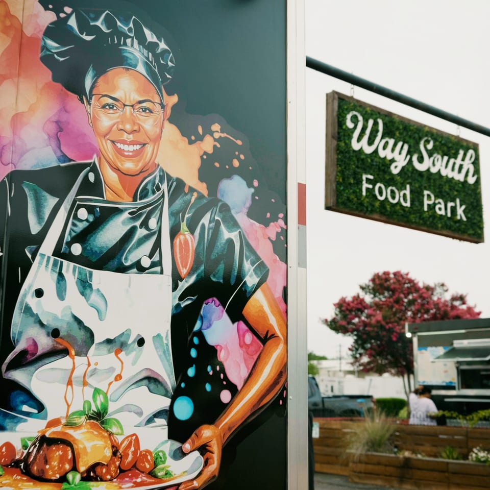 Colorful mural of a smiling chef holding two plates of food next to a "Way South Food Park" sign.