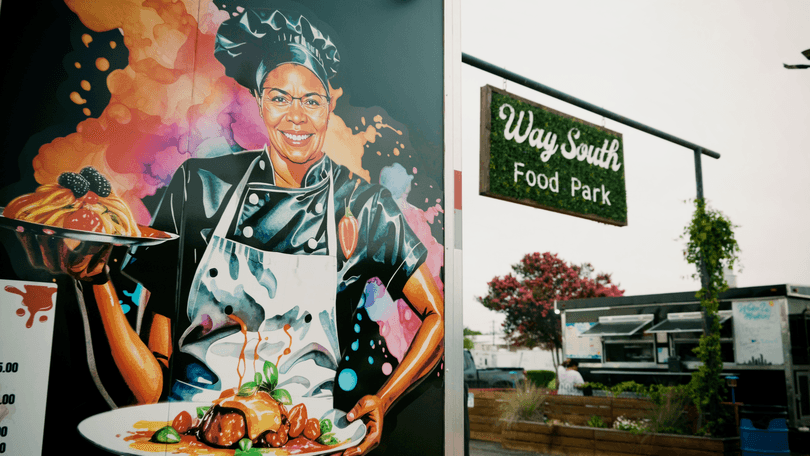 Colorful mural of a smiling chef holding two plates of food next to a "Way South Food Park" sign.