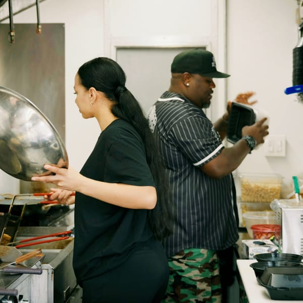 Two chefs, a woman and a man, working in a busy commercial kitchen with stainless steel equipment.