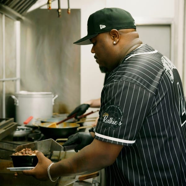A chef in a Ruthie's branded shirt preparing food in a busy kitchen.