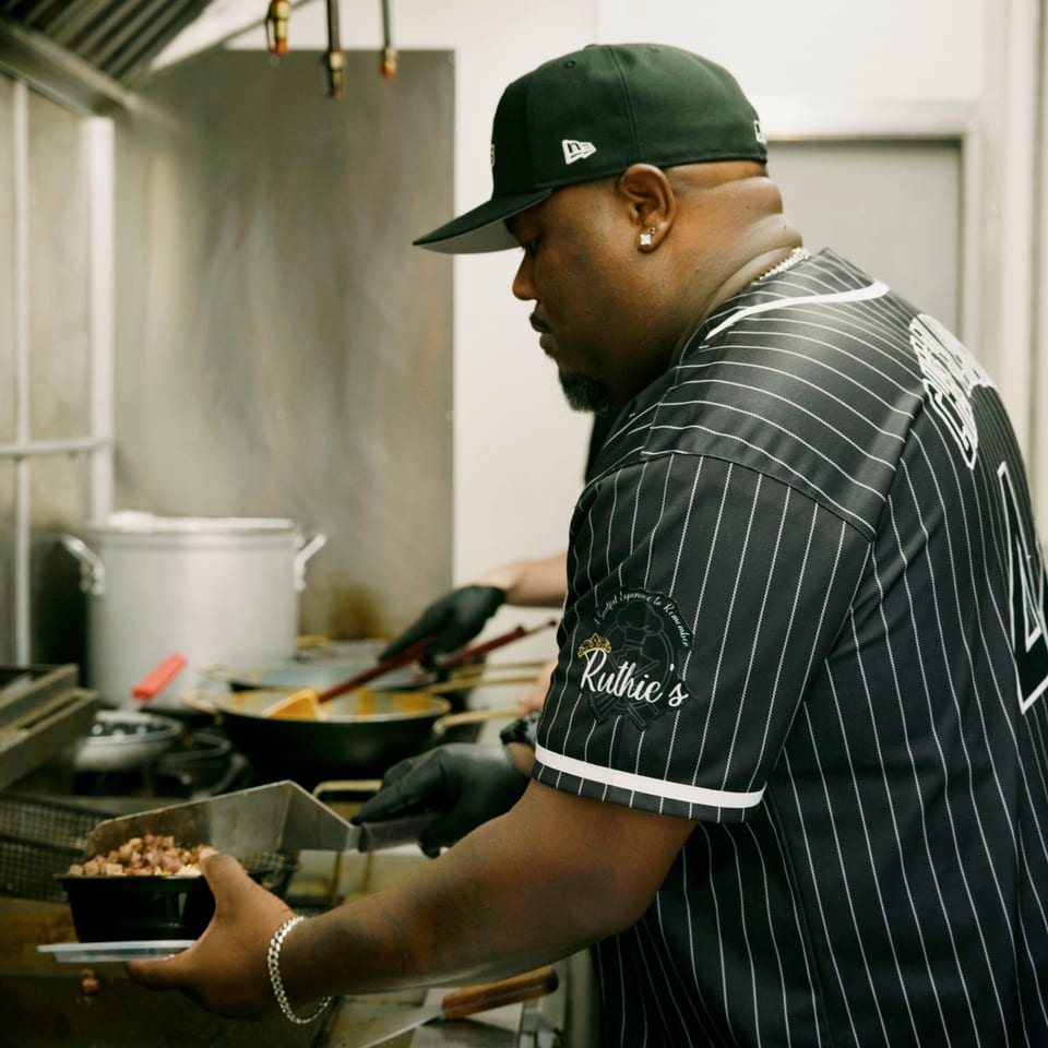 A chef in a Ruthie's branded shirt preparing food in a busy kitchen.