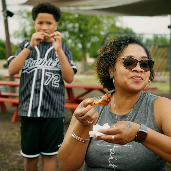 A woman and boy eating chicken wings at an outdoor picnic table.