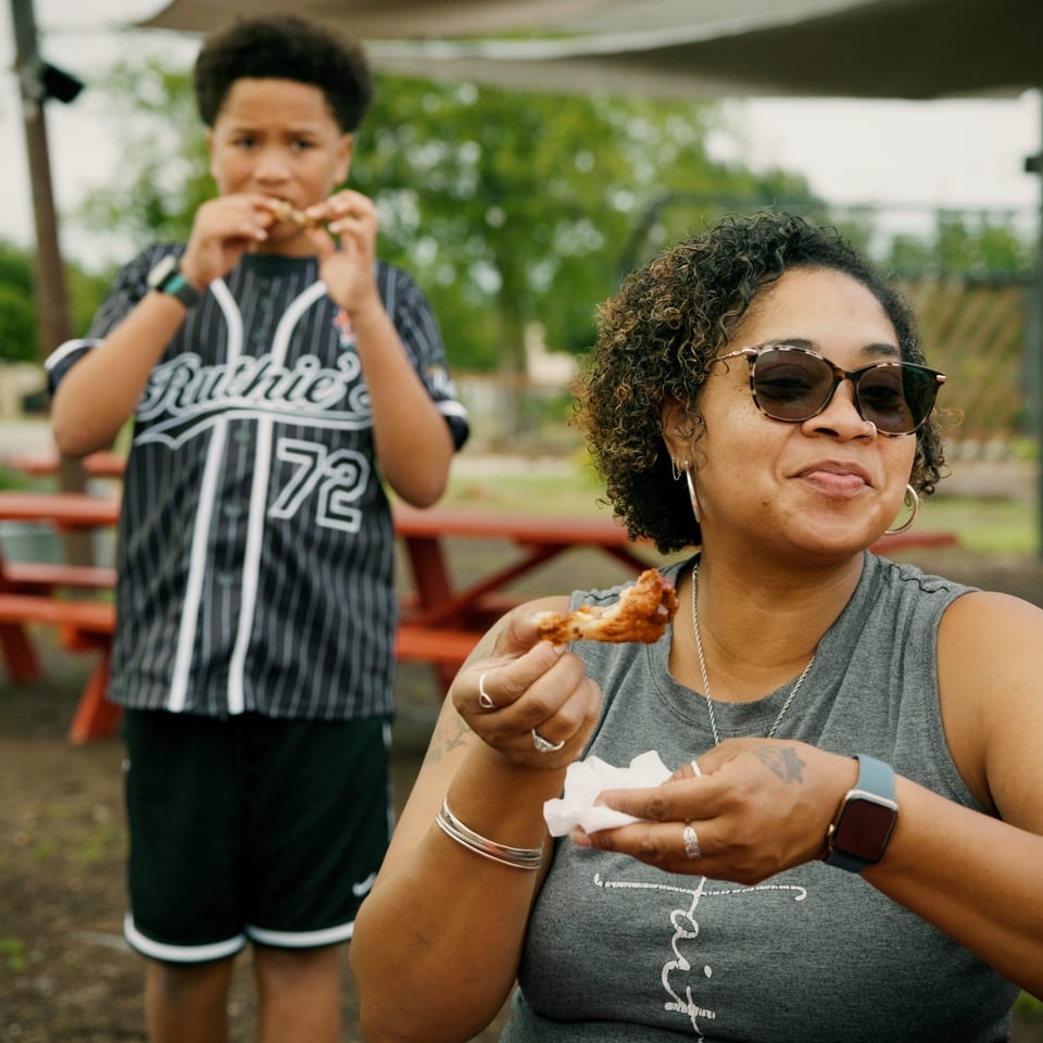 A woman and boy eating chicken wings at an outdoor picnic table.
