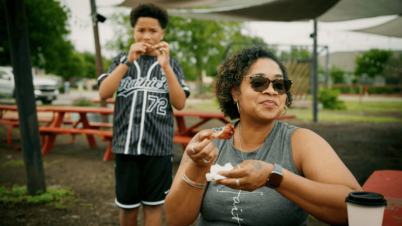 A woman and boy eating chicken wings at an outdoor picnic table.